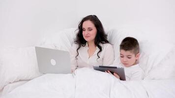 mom and son under blanket playing on tablet laugh smile games internet online learning educational activities spend time together in the family at home recover skip school at kindergarten day off video