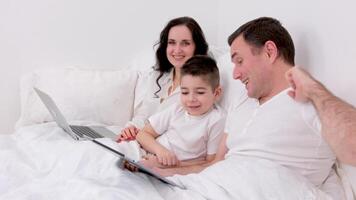 husband wife and son spend time together in bed holiday look at tablet communicate conversation love at home happiness joy success in gadgets white background place for advertising text happy family video
