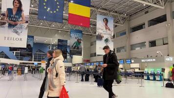 rumänien bukarest flygplats 2024-04-20 passagerare under en stor Land flagga i de avresa område av henri coanda otopeni internationell flygplats. video