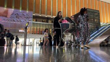 doha aeroporto Qatar 16.05.2024 arabo donne con bambini e passeggini negozi boutique persone in viaggio in attesa per loro aereo mossa a partire dal terminale per un altro terminale nel il riposo la zona video