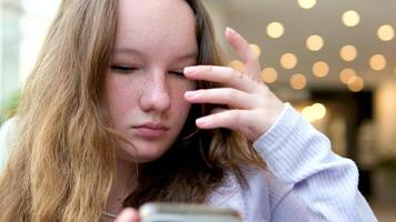 schön Weiß blond Teenager Modell- Mädchen, sehr hübsch, lächelnd, natürlich suchen, draußen tragen Weiß Jacke zeigen das Smartphone auf das Kamera halten es im Gerade Hand. Handy, Mobiltelefon Telefon im Hand video