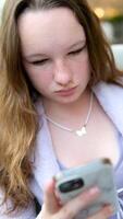 Young girl walking in park and talking by smartphone near tree in blossom. Concept of modern technology and spring in nature. video