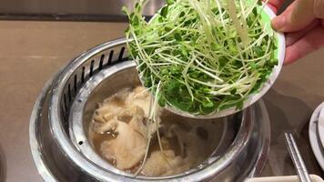 Woman adding fresh microgreens into bowl with tasty leek soup at wooden table, closeup video