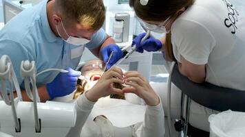 mulher mostrando coração com mãos profissional dente limpeza dentista com assistente debaixo microscópio guloseimas a pacientes dentes. moderno progressivo odontologia. video