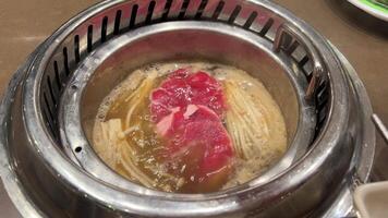 Add raw meat to boiling soup broth in a pan in Vietnam buffet selection of dishes cooking on the table video
