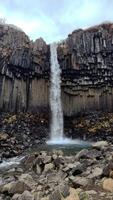 A wide vertical view captures a waterfall cascading down hexagonal basalt columns video