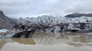 A glacier front partially melted into a lake, framed by distant mountains video