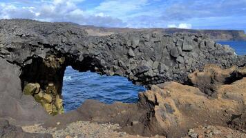 un detallado ver de un arco rock formación en un negro arena playa en Islandia. video