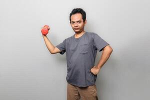 a handsome Asian man in gray is passionately lifting red dumbbells with a serious face photo