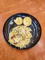 un plato de espaguetis carbonara con dos rebanadas de ajo un pan en el mesa. adecuado para italiano comida menú contenido foto