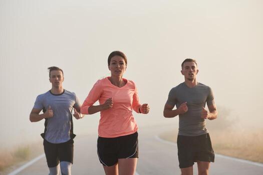 A group of friends, athletes, and joggers embrace the early morning hours as they run through the misty dawn, energized by the rising sun and surrounded by the tranquil beauty of nature photo