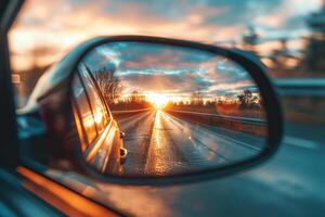 The setting sun on the side mirror of car. Beautiful landscape and road visible in the mirror photo