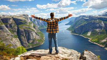hombre soportes en el borde de acantilado con su brazos extendido y mira a hermosa paisaje con montañas y río foto