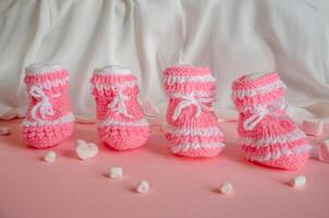 Pink knitted booties on pink background with marshmallow hearts. High quality photo