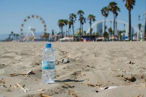 Bottle of drinking water stands on not very clean beach. There is a Ferris wheel on the background. photo