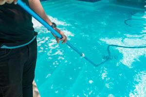 persona limpieza un nadando piscina con un vacío manguera. hombre limpieza nadando piscina con succión manguera foto