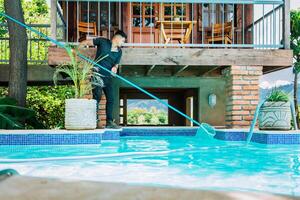 Man cleaning swimming pool water with a skimmer. Maintenance person cleaning the leaves of a pool with the skimmer photo