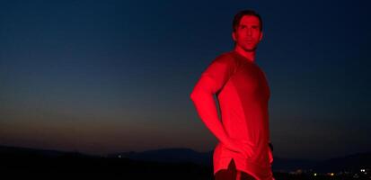 atleta huelgas un actitud debajo rojo Noche resplandor después intenso todo el día maratón. foto