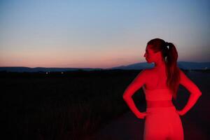 atleta huelgas un actitud en iluminado en rojo Noche resplandor foto