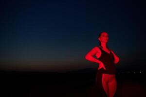 atleta huelgas un actitud en iluminado en rojo Noche resplandor foto