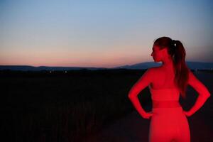 atleta huelgas un actitud en iluminado en rojo Noche resplandor foto