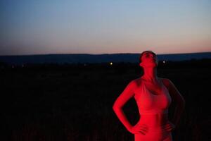 atleta huelgas un actitud en iluminado en rojo Noche resplandor foto