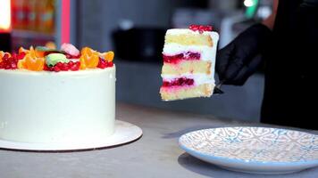 A piece of cake is taken with a spatula by hands in black gloves and placed on a dish. The top of the white cake is decorated with berries. Close up video