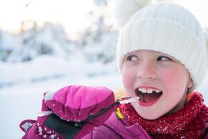 Cute little girl while eating icicle on beautiful winter day photo