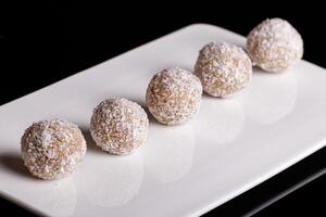 Beautiful sweets with coconut on a white plate on a black background photo