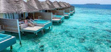 Aerial view of Maldives island, luxury water villas resort and wooden pier. Beautiful sky and ocean lagoon beach background. Summer vacation holiday and travel concept. Paradise aerial landscape pano photo