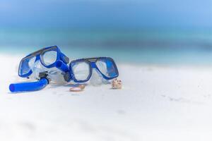 Summer beach scenery with snorkel gear, googles on soft sand with calm waves splashing. Tropical summer beach landscape, vacation or holiday concept. Relaxing view of recreational activity, snorkeling photo