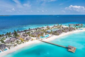 Aerial view of Maldives island, luxury water villas resort and wooden pier. Beautiful sky and ocean lagoon beach background. Summer vacation holiday and travel concept. Paradise aerial landscape pano photo