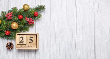 christmas tree branch with toys and gifts and wooden calendar december 25 on wooden background photo