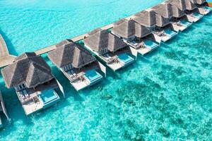 Aerial view of Maldives island, luxury water villas resort and wooden pier. Beautiful sky and ocean lagoon beach background. Summer vacation holiday and travel concept. Paradise aerial landscape pano photo