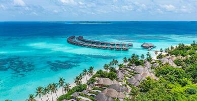 Aerial view of Maldives island, luxury water villas resort and wooden pier. Beautiful sky and ocean lagoon beach background. Summer vacation holiday and travel concept. Paradise aerial landscape pano photo