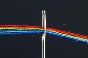 multi-colored threads for sewing in the form of a rainbow pass through an antique needle on a black background photo