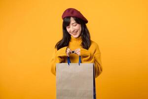 Young Asian woman in her 30s, wearing a yellow sweater and red beret, enjoys a shopping spree against a vibrant yellow background. photo