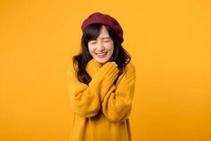 Shy young Asian woman in her 30s, crossing her arms on her chest with a subtle smile, wearing a yellow sweater and red beret against a yellow background. photo