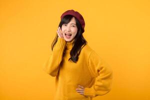 Young Asian woman in her 30s making a stylish announcement, wearing a yellow sweater and red beret against a vibrant yellow background. Expressive and dynamic communication. photo