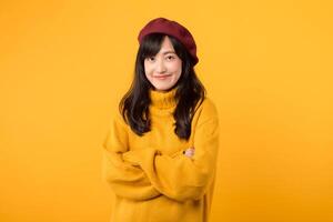 Confident young Asian woman in her 30s, crossing her arms on her chest with a cool smile, dressed in a yellow sweater and red beret against a yellow background. photo