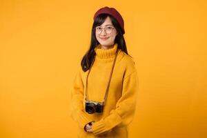 In her cheerful studio, a young Asian woman, wearing a yellow sweater and red beret, snaps pictures with her camera, embracing the joy of photography. photo