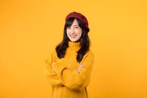 Satisfied young Asian woman in her 30s, confidently crossing her arms on her chest, dressed in a yellow sweater and red beret against a yellow background. photo