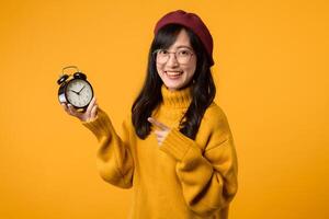 In a cheerful scene, a young woman in a yellow sweater and red beret shows off her alarm clock, embodying punctuality and success. photo