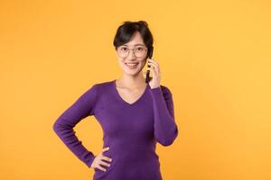 happy, young lady with a smartphone, wearing a purple shirt and eyeglasses, expressing joy through online shopping and social interactions. Embrace the digital age against a yellow background photo
