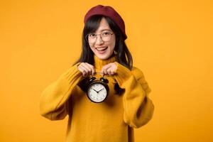 In a cheerful scene, a young woman in a yellow sweater and red beret holds an alarm clock, ready to face the morning. photo