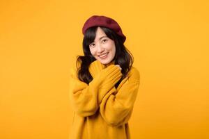 Confident young Asian woman in her 30s, crossing her arms with a cool and stylish expression, donning a yellow sweater and red beret against a yellow background. photo