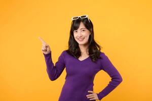 Beautiful young Asian woman 30s wearing purple shirt pointing up to copy space with smile face and happy. Pretty girl act like a satisfied product, use for advertising with yellow background photo