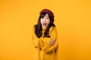 Surprise young Asian woman in her 30s, crossing her arms on her chest, wearing a yellow sweater and red beret against a yellow background. photo