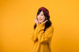 Young Asian woman in her 30s, shyly crossing her arms on her chest, exuding charm in a yellow sweater and red beret against a yellow background. photo