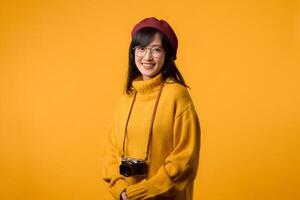 con su cámara, un joven asiático mujer, puesto en un amarillo suéter y rojo boina, toma un retrato, exhibiendo su artístico buscar. foto